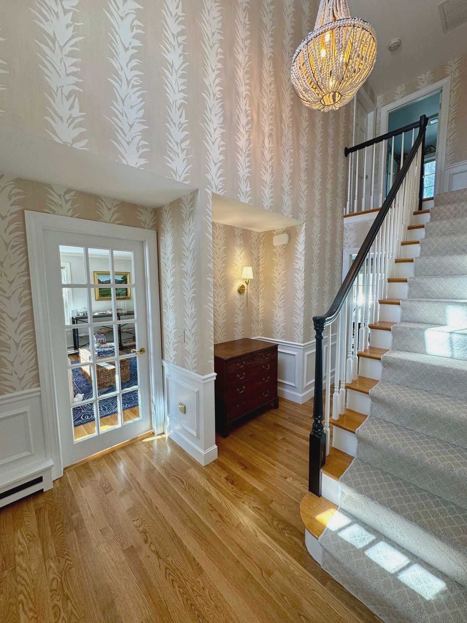 Bright foyer with wood floors, staircase, chandelier, and glass-paned door leading outside.