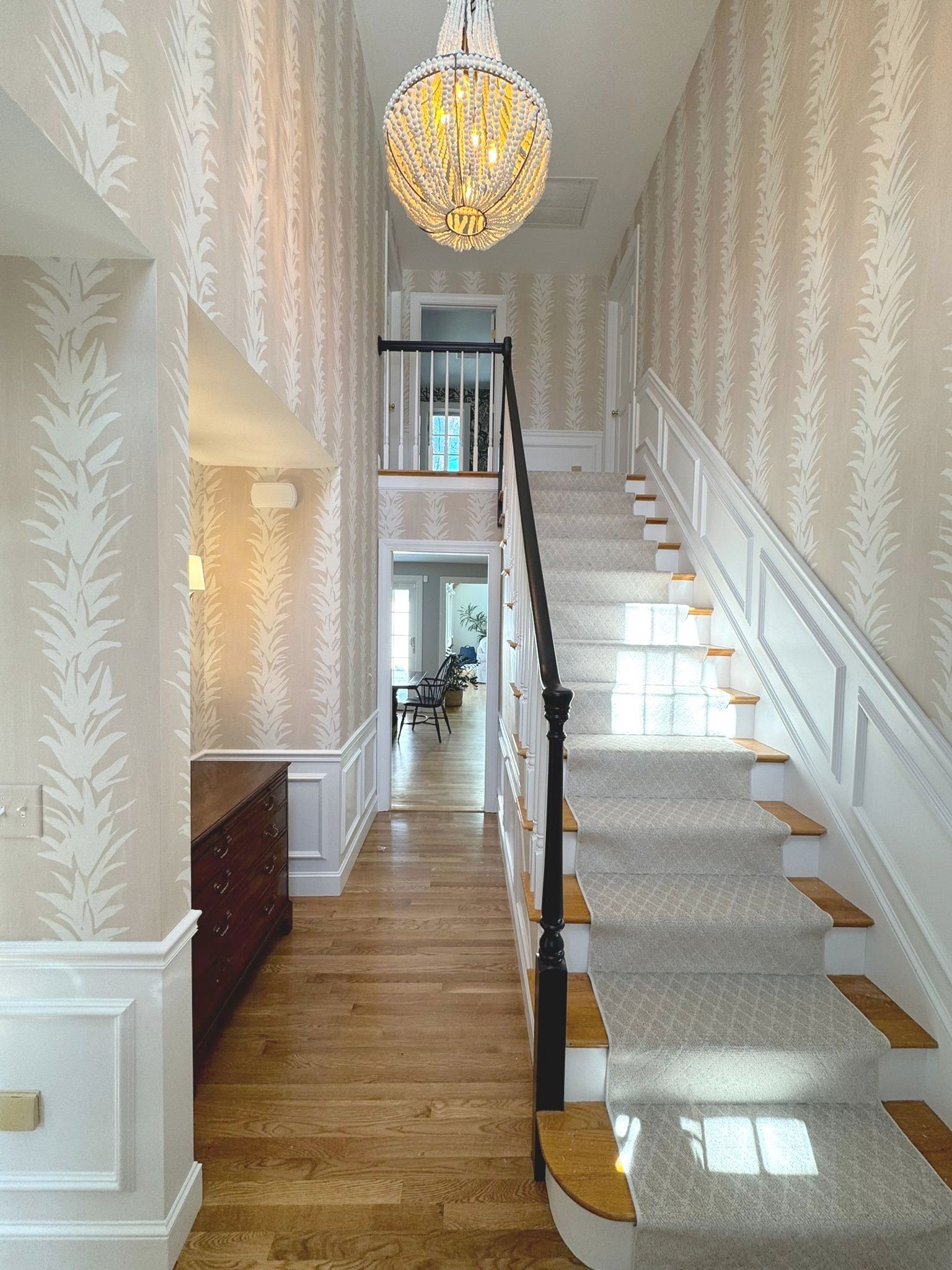 Elegant foyer with staircase, chandelier, and polished wood floors leading to a lower hallway.