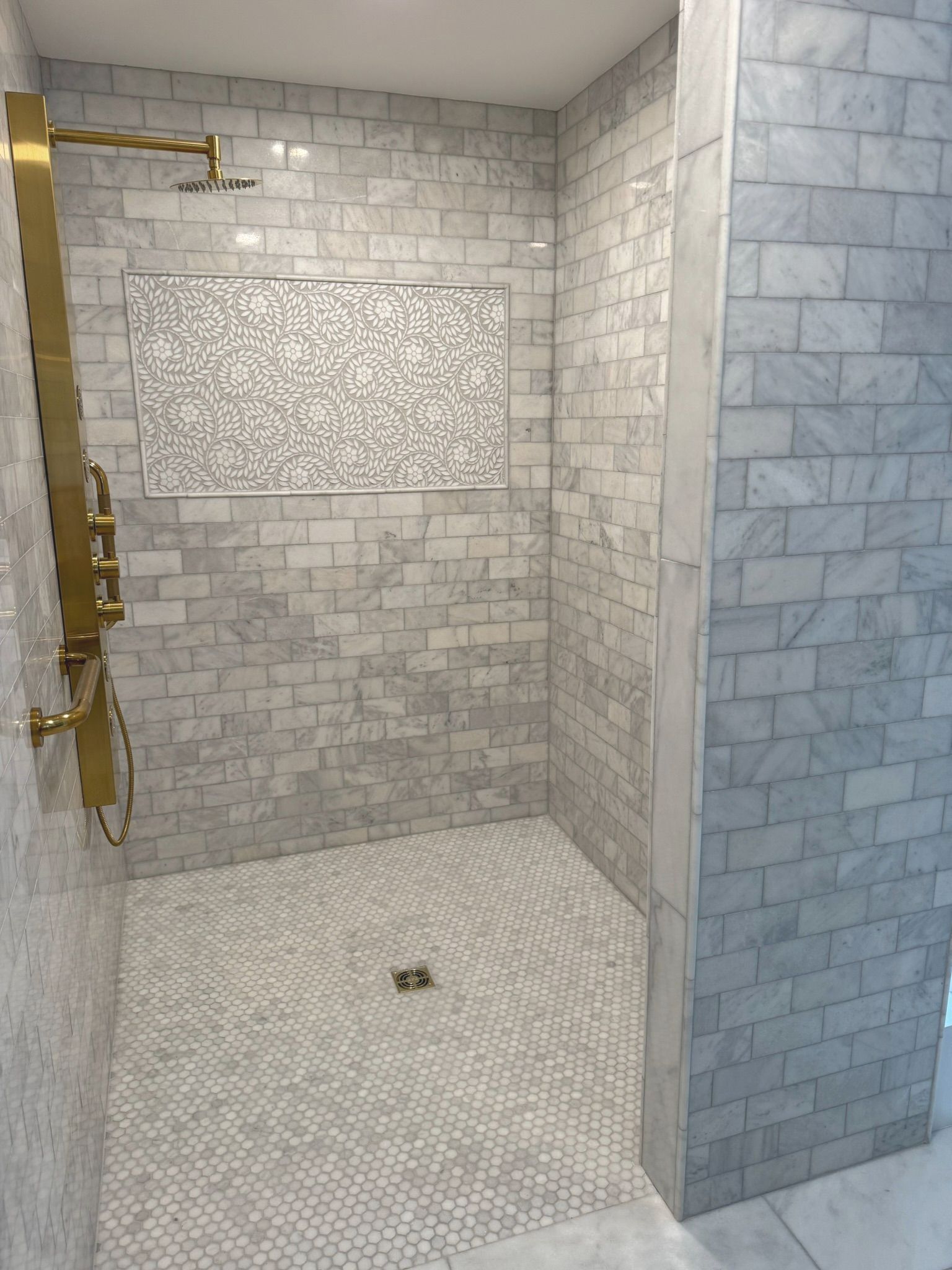 White-tiled walk-in shower with brass fixtures and mosaic floor drain.
