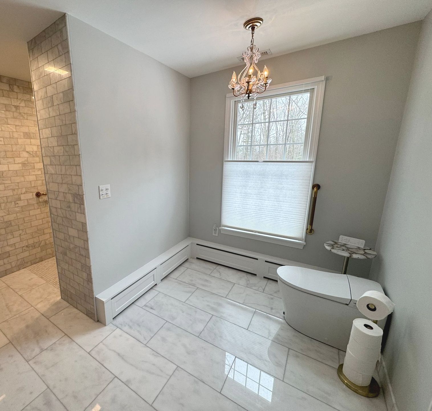Small bathroom with white tile, toilet, window, chandelier, and a raised tub or shower area.