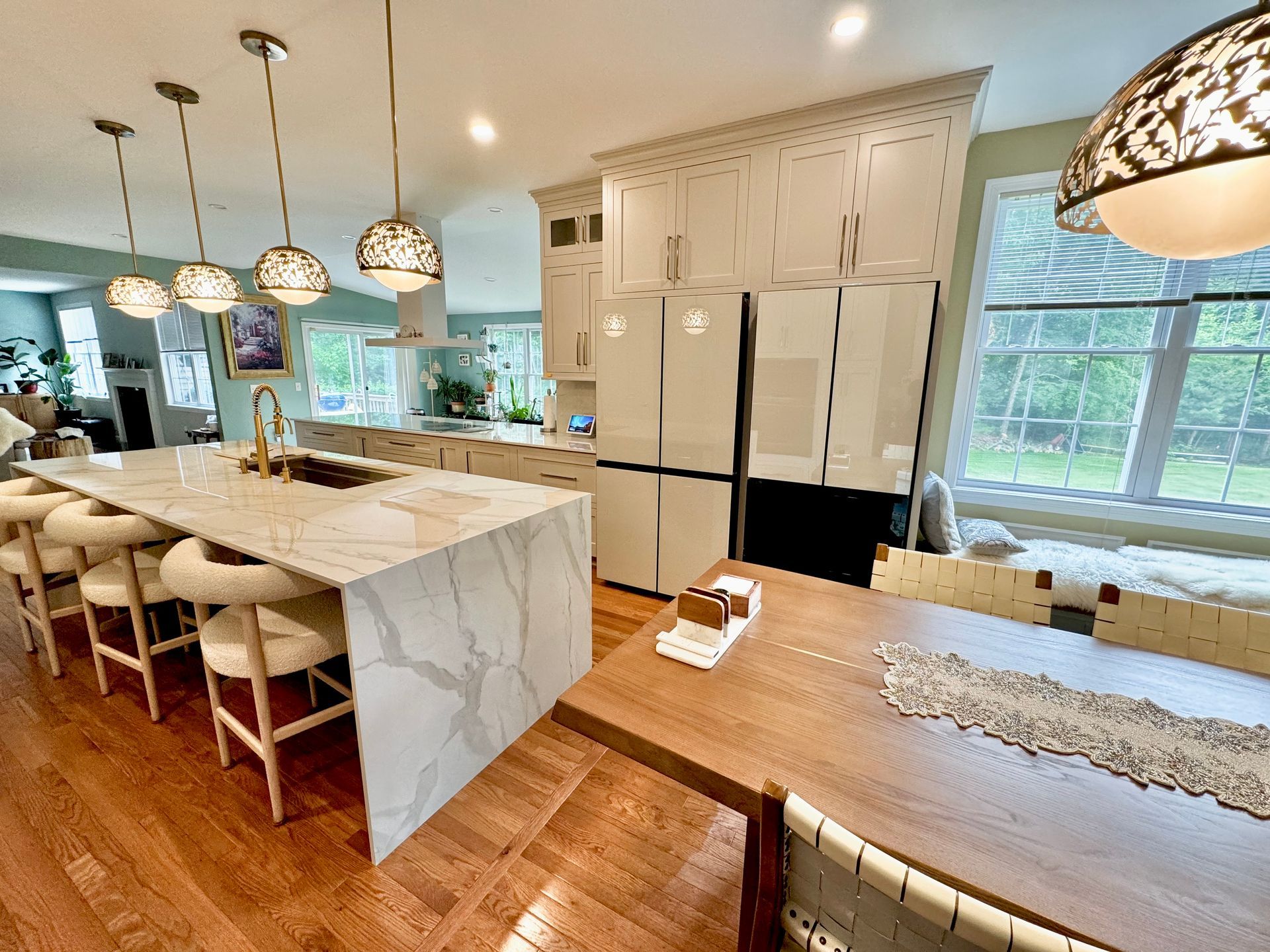 Bright kitchen with marble island, white cabinets, dining table, and large windows