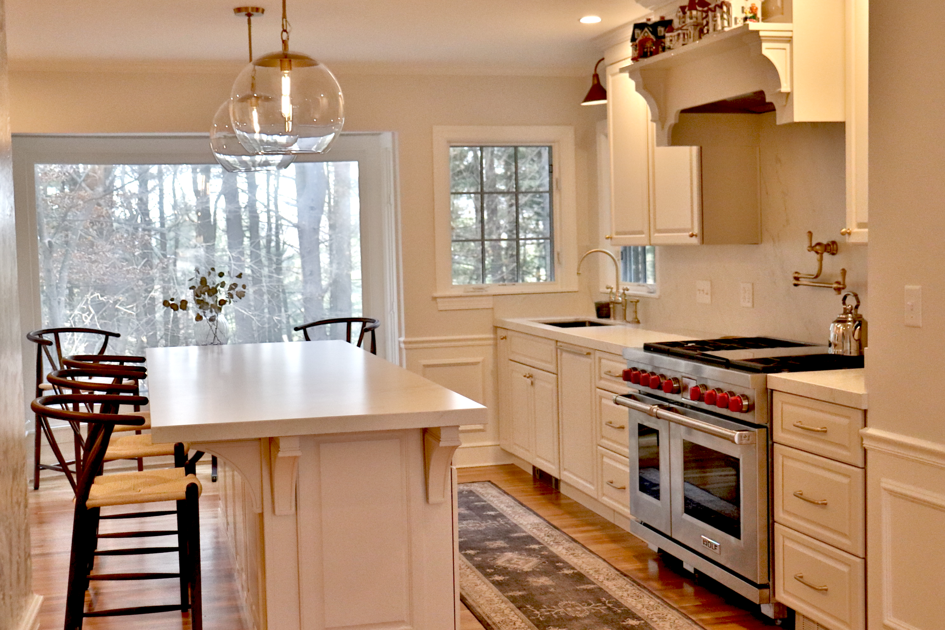 Bright modern kitchen with white cabinets, large island, stove, and dining table by a snowy window