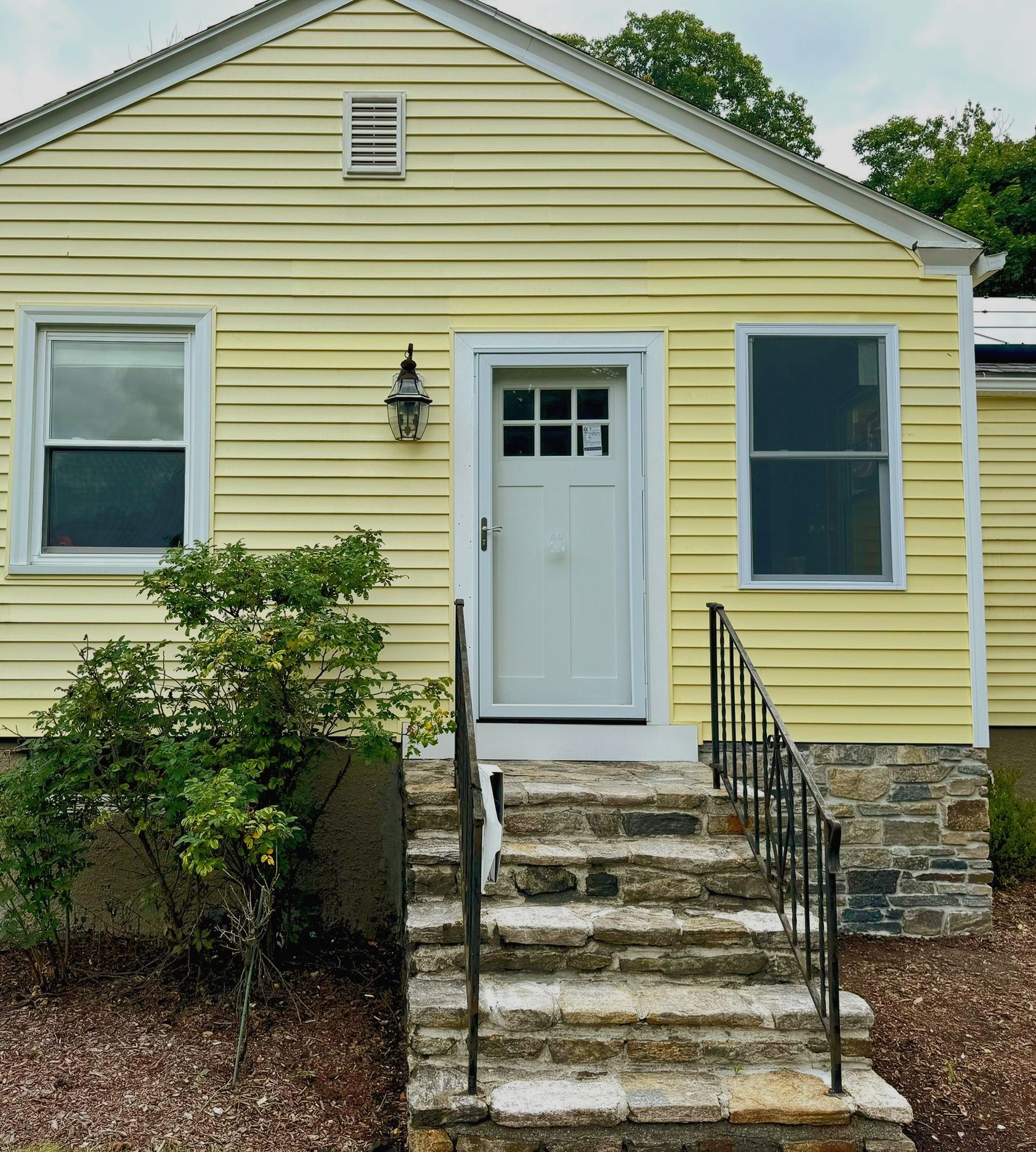 Yellow house front with white door, stone steps, and black railings.