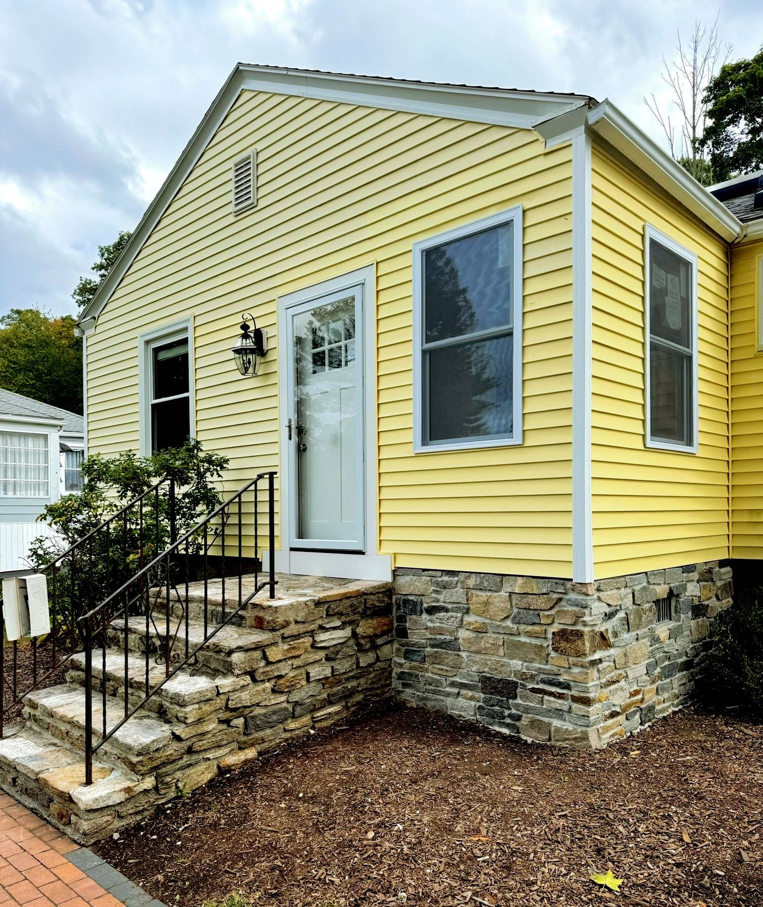 Yellow house with stone foundation, front steps, and white door