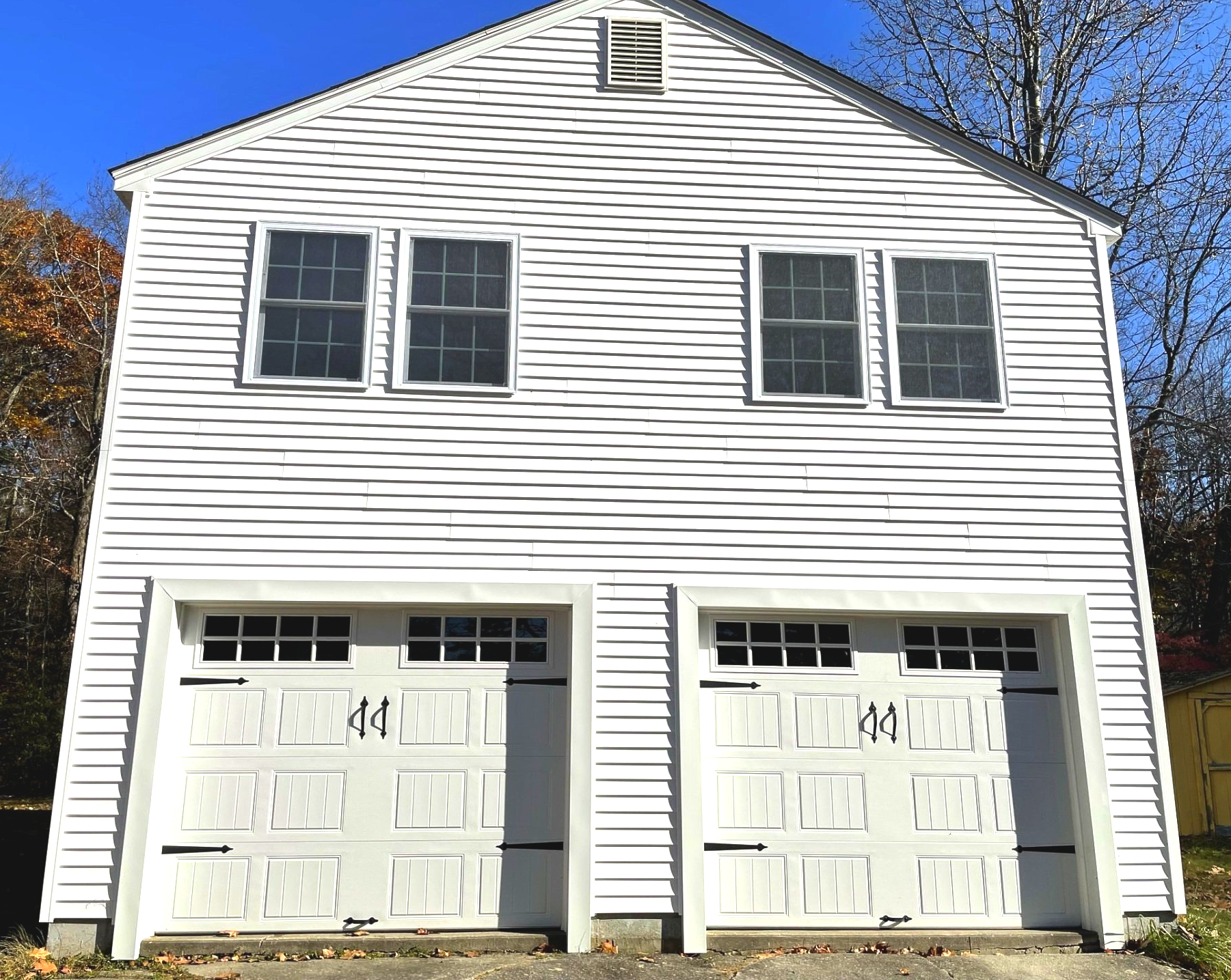 White two-story house with two white garage doors and four windows under a blue sky.
