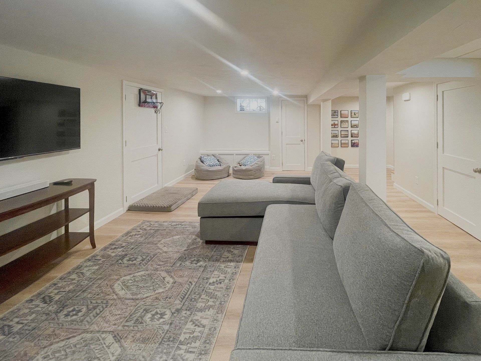 Modern living room with gray sectional sofa, patterned rug, wall-mounted TV, and white walls