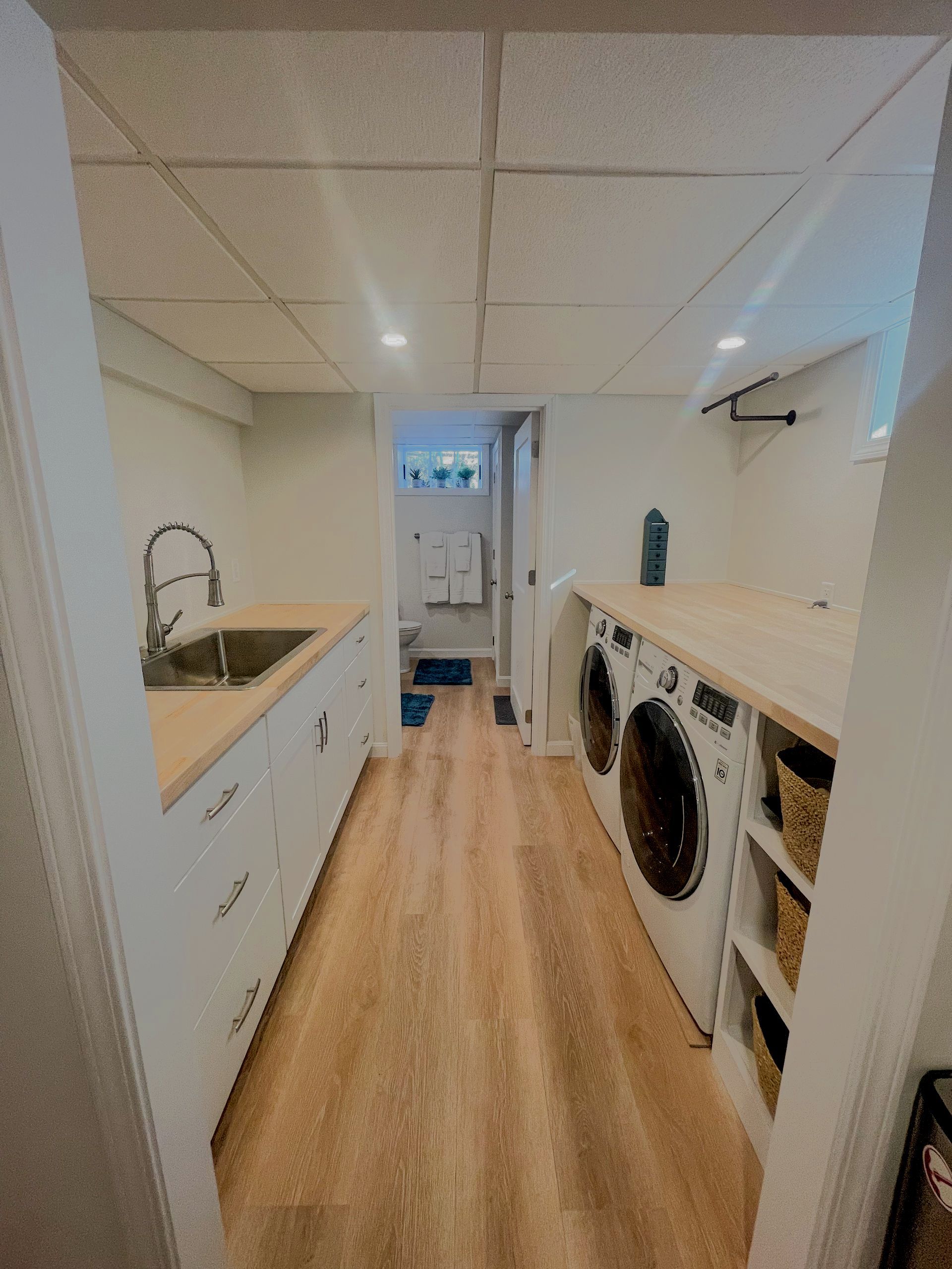 Bright laundry room with sink, washer and dryer, wood floor, and a doorway at the end