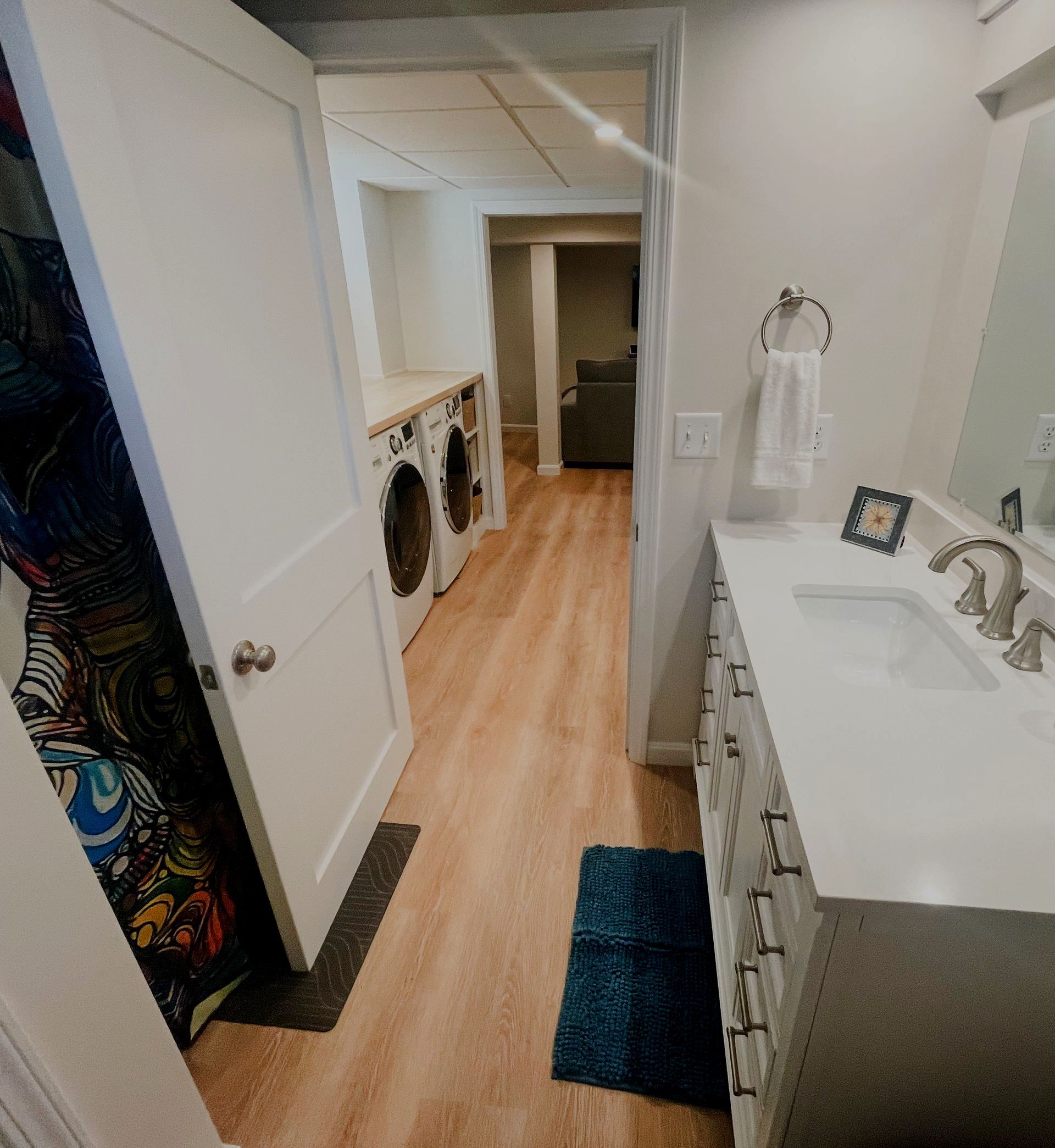 Bright bathroom with white vanity, tub, and open door leading to a hallway with hardwood floors.