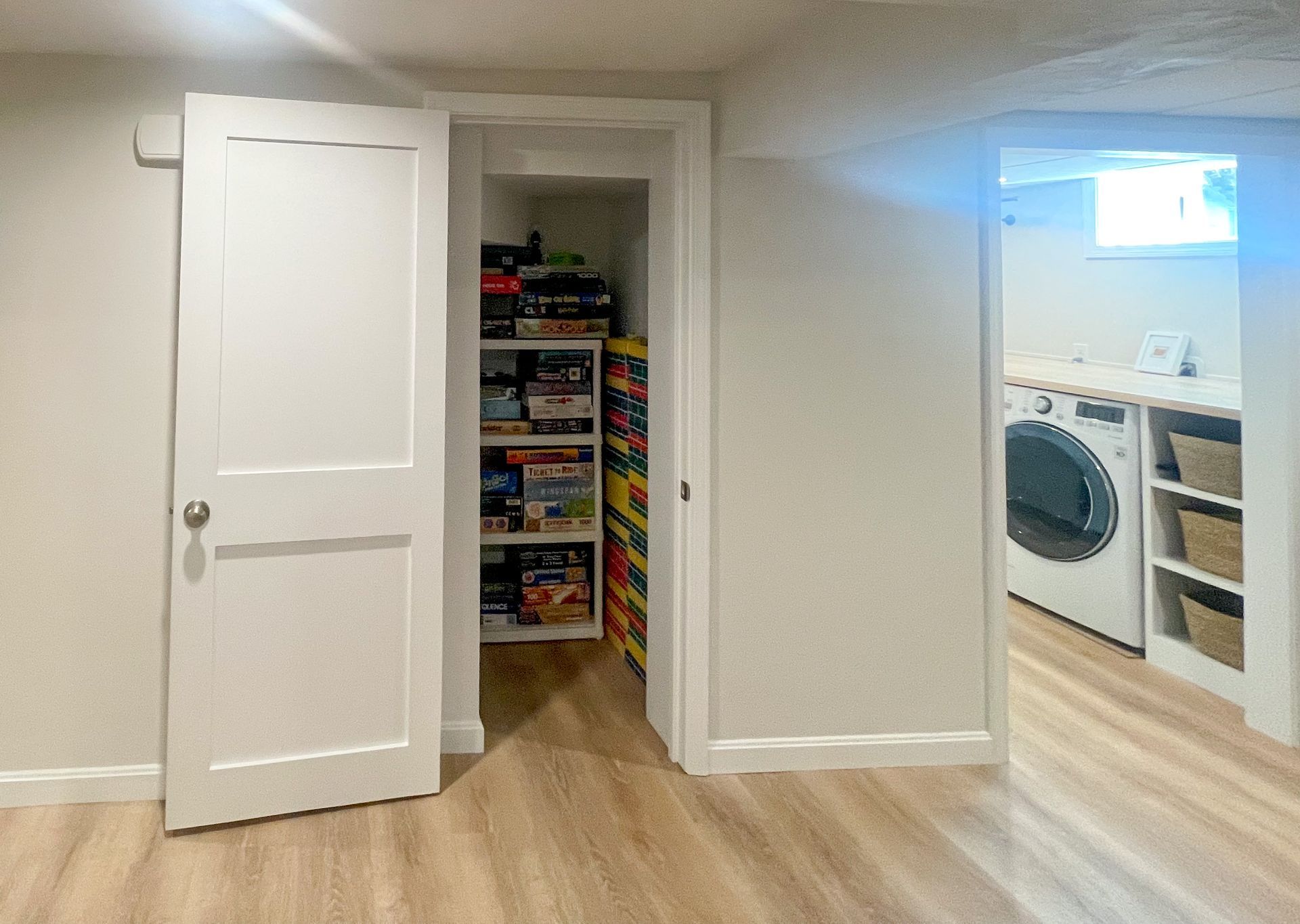 White hallway with open closet of toys and a partial view into a laundry room on the right.