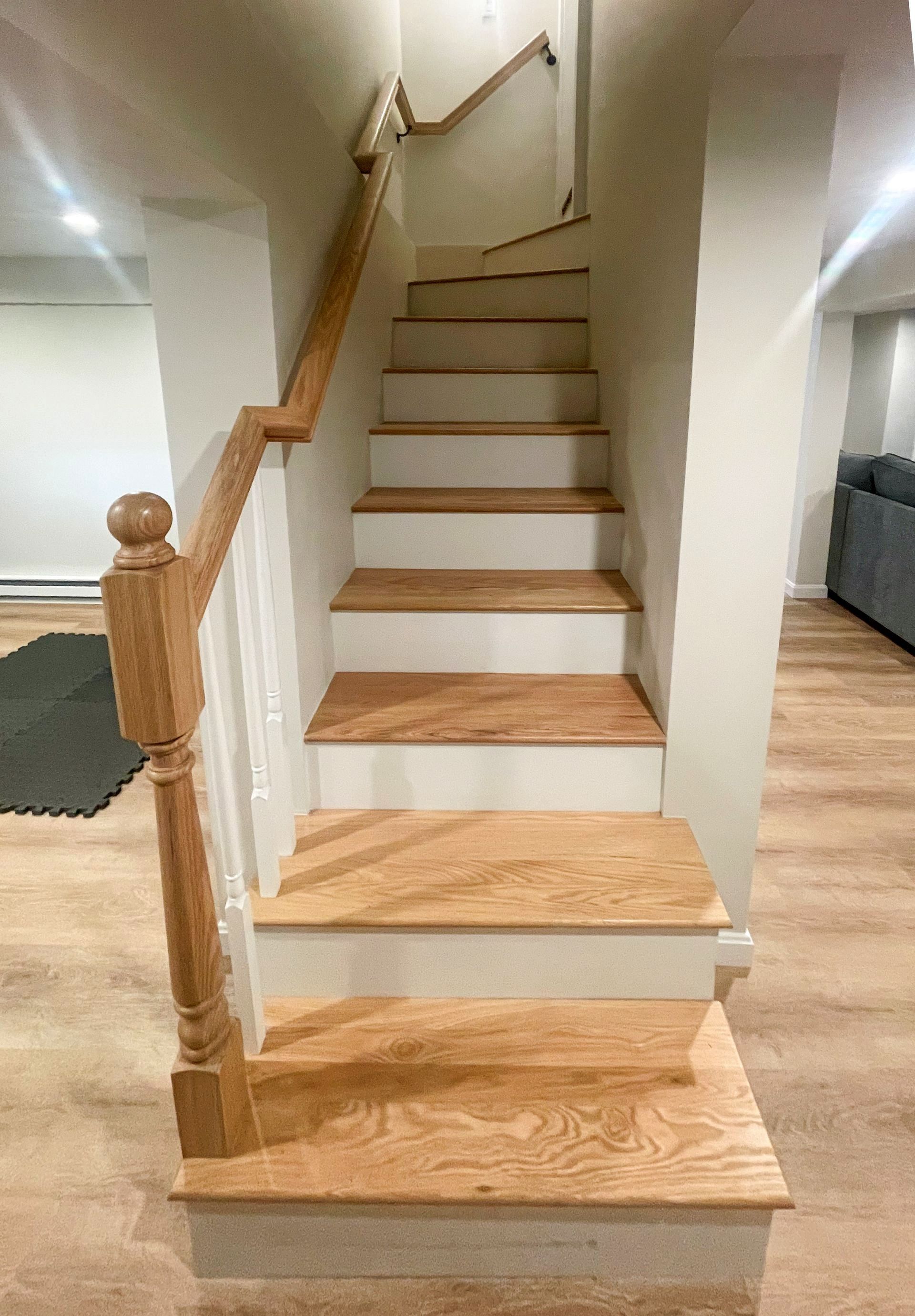 Indoor wooden staircase with beige carpeted steps and a railing, leading to an upper floor hallway