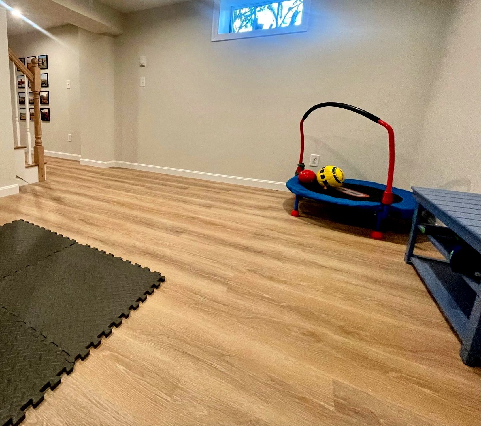 Empty playroom with wood floor, foam mat, small ball pit, and low window.