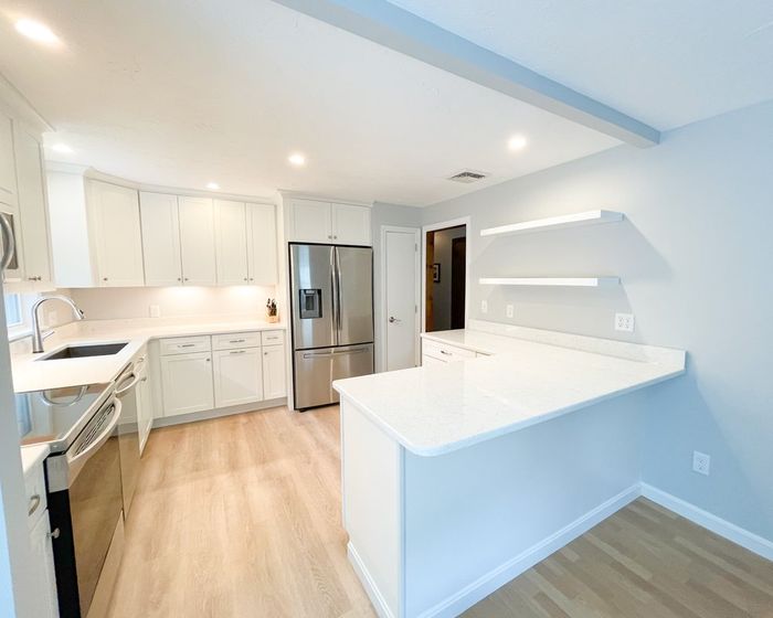 A kitchen with white cabinets , stainless steel appliances , a refrigerator and a sink.