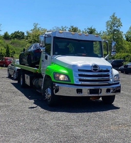 Green and white tow truck parked on gravel under a blue sky
