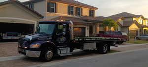 Dark flatbed tow truck parked on a suburban street in front of houses at dusk