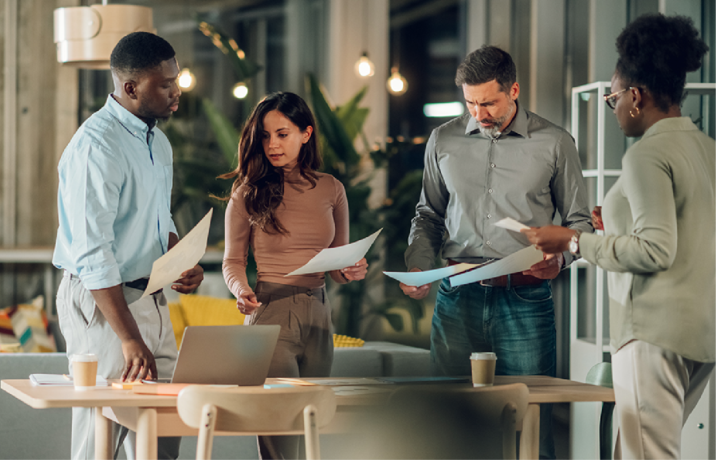 A diverse professional team collaborates around a table in a modern office, reviewing documents and discussing work.