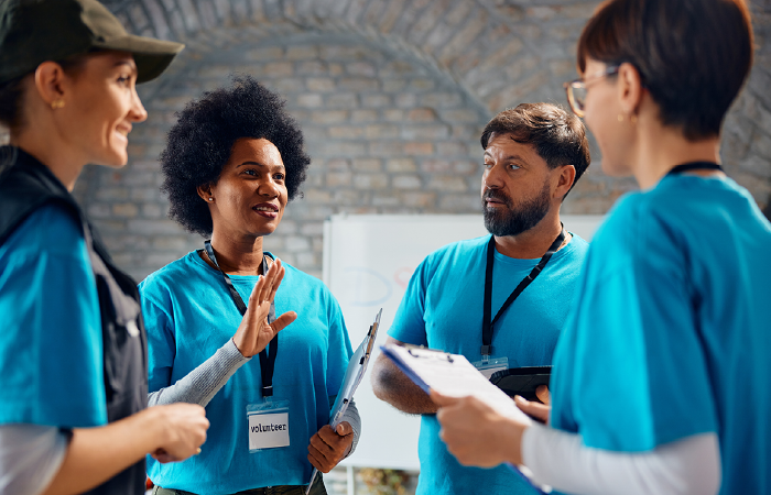 A group of four individuals in matching blue volunteer shirts discussing work in a room with a brick wall.