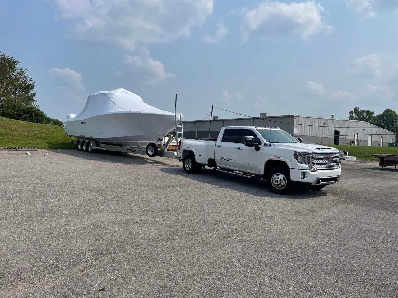 White boat on trailer hitched to a white pickup in a gravel lot under a cloudy sky