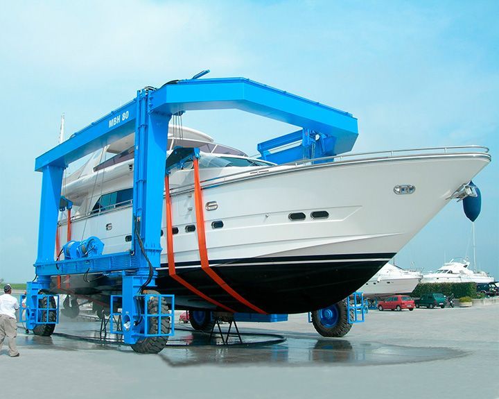 White yacht lifted by a blue marine hoist on a dockside lot
