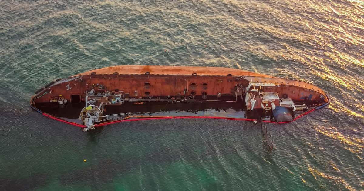A rusted cargo ship wrecked in shallow water, seen from above.