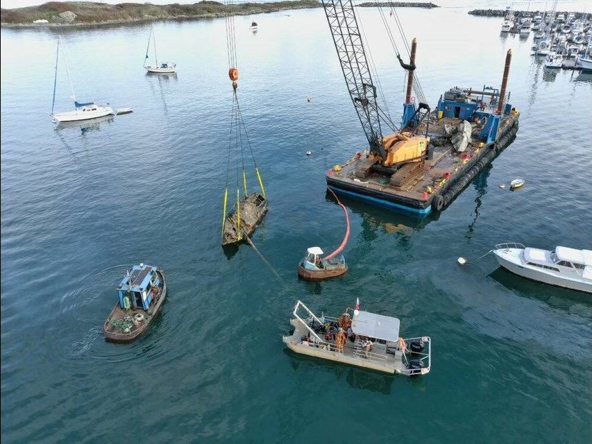 Boats and a crane barge working on calm blue water in a harbor