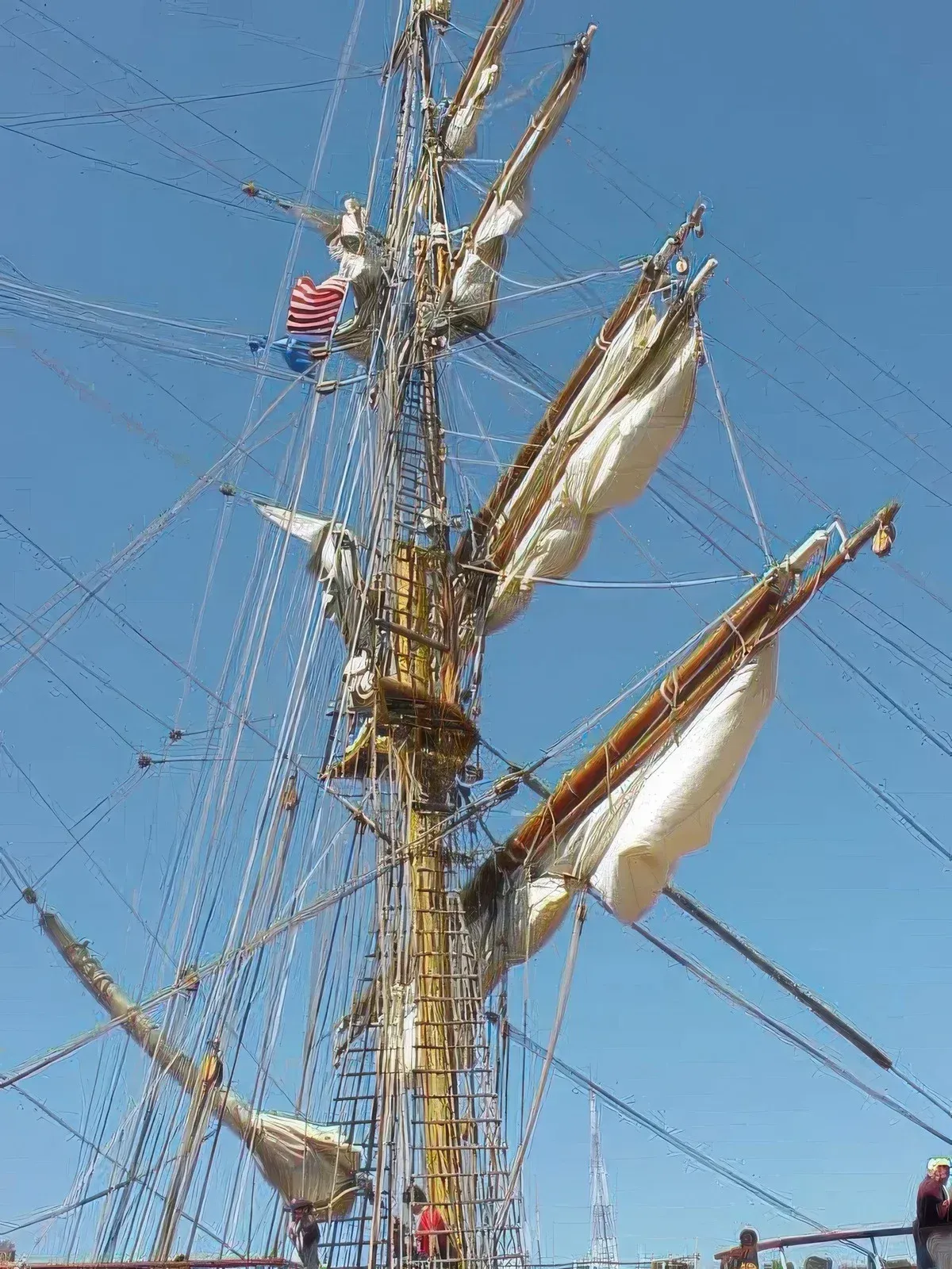 Tall sailing ship mast with rigging and white sails against a blue sky