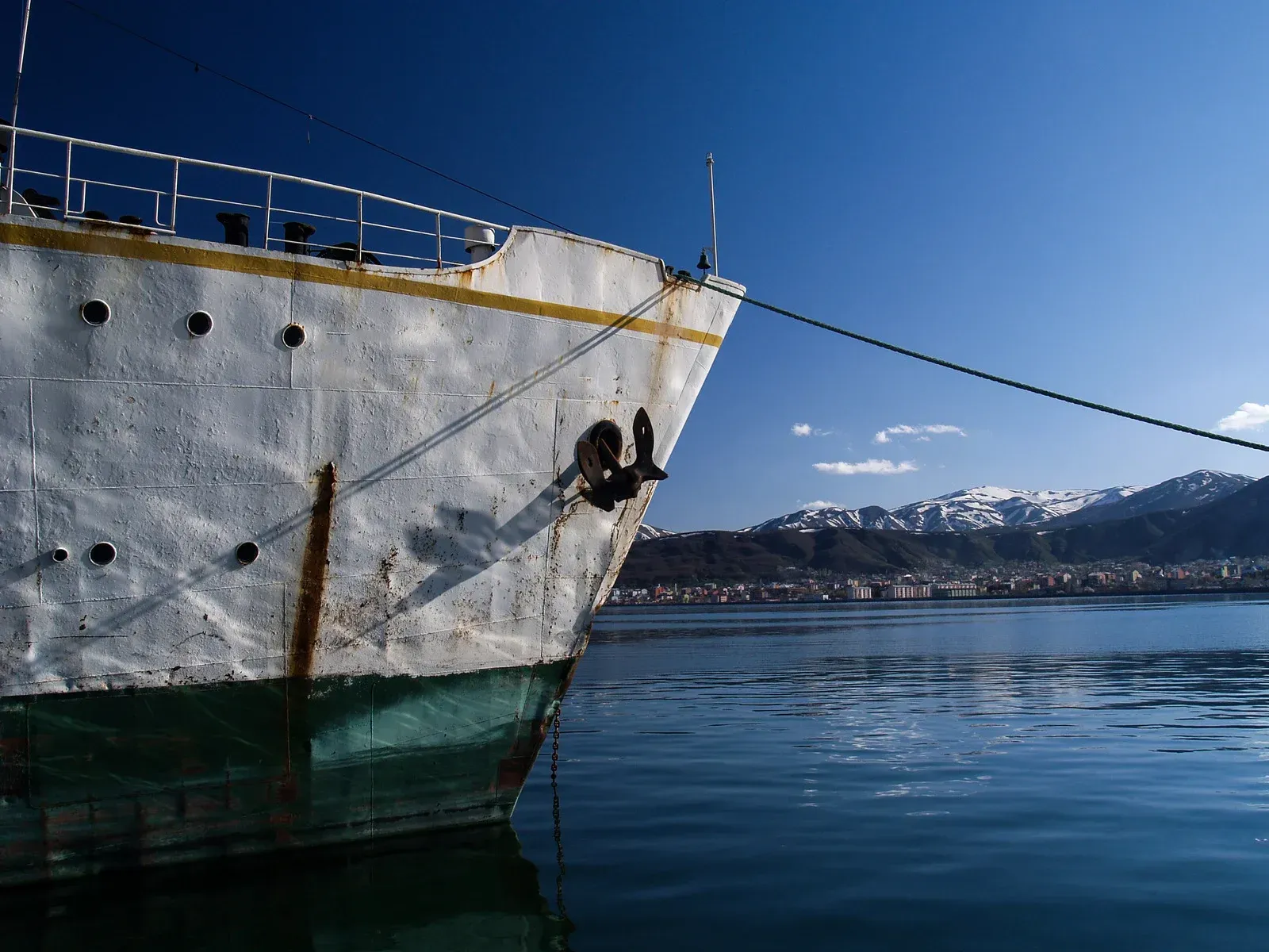 Large white ship bow beside calm blue water with snowy mountains in the distance