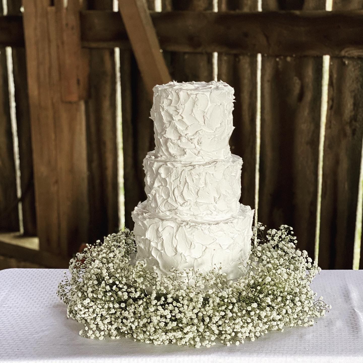 Three-tier white wedding cake with baby’s breath on a table in a rustic wooden setting