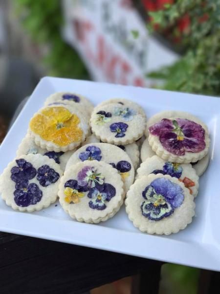 White plate of floral-decorated cookies with purple and yellow edible flowers outdoors