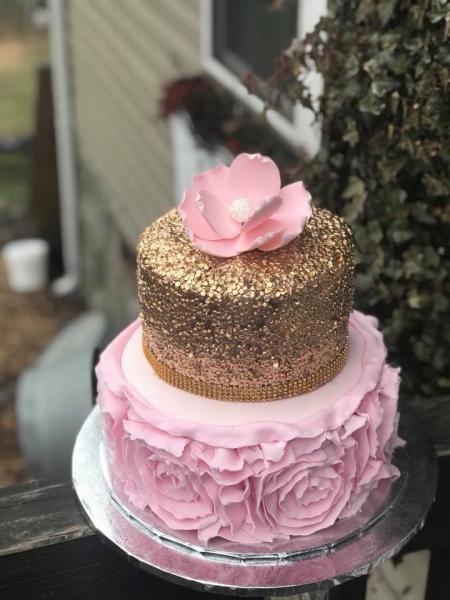 Two-tier pink and gold cake with a pink flower topper on a glass stand