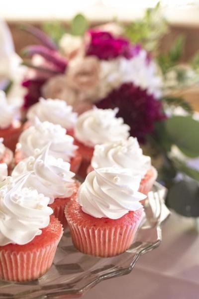 Pink cupcakes with white frosting on a glass platter, with blurred flowers in the background