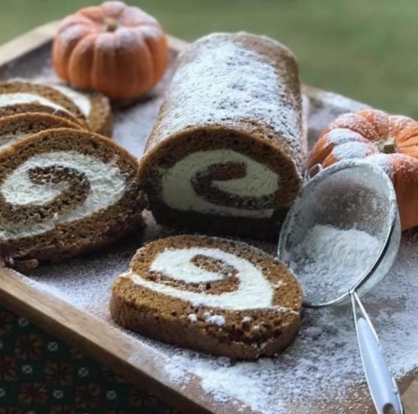 Chocolate Swiss roll dusted with powdered sugar on a wooden tray, with small pumpkins and a spoon