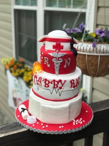 Red and white baby shower cake with rattle and teddy bear decorations on a table outdoors