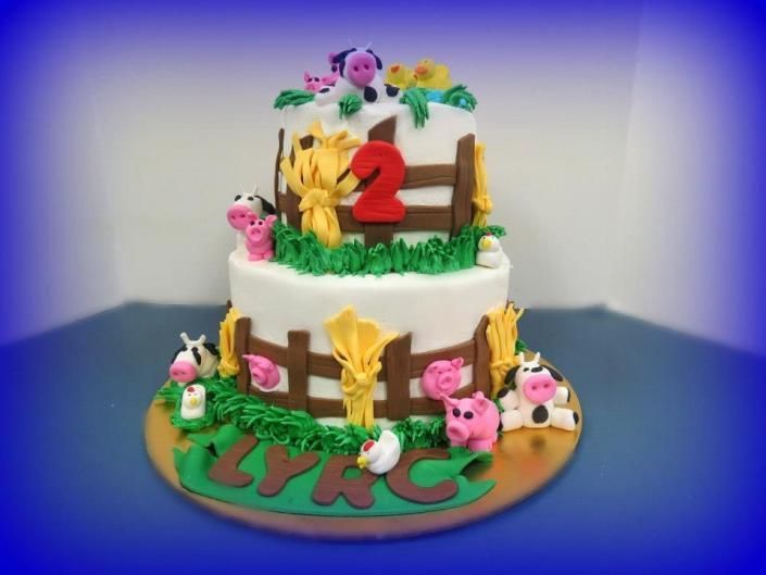 Two-tier birthday cake with red number 2, flowers, and cartoon pig decorations on a green base