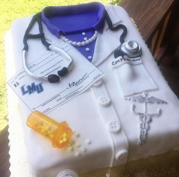 Decorated white cake shaped like a doctor’s coat with a stethoscope, pills, and medical symbols