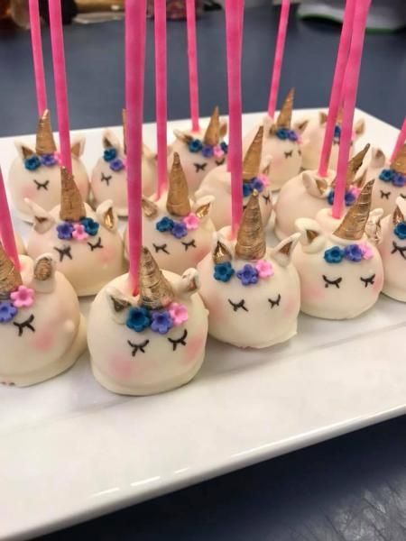Plate of white unicorn cake pops with pink horns, blue eyes, and gold ears on sticks