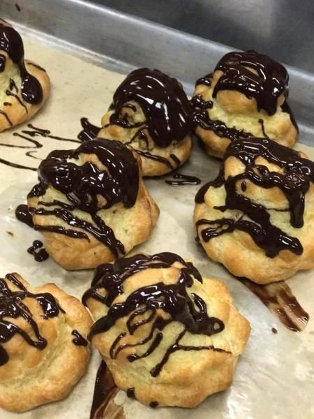 Tray of small cream puffs drizzled with chocolate on a baking sheet