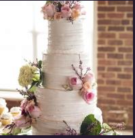 White tiered wedding cake with pink and green floral decorations on a table