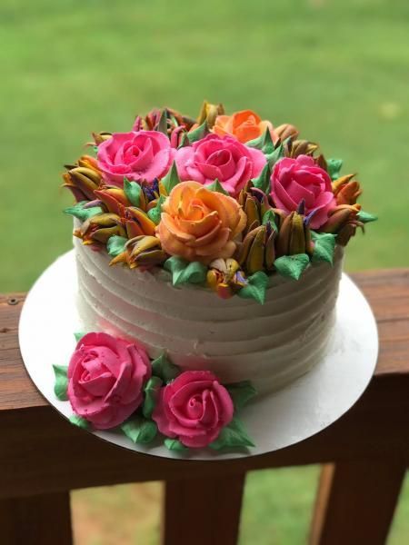 Round cake topped with pink and orange roses on a white plate atop a wooden table