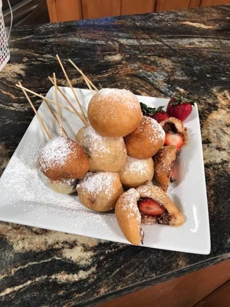 Plate of powdered sugar-dusted fried pastries with strawberry filling on wooden skewers on a countertop