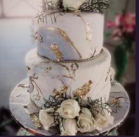Two-tier white wedding cake with gold accents and white roses on a silver cake board