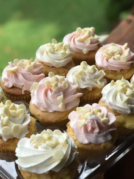 Tray of frosted cupcakes with white and pink swirled icing on a blurred green background