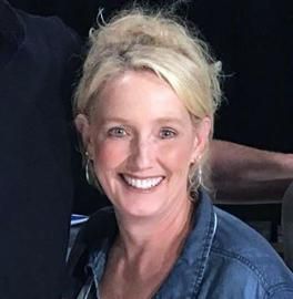 Smiling blonde woman in a denim shirt against a dark background