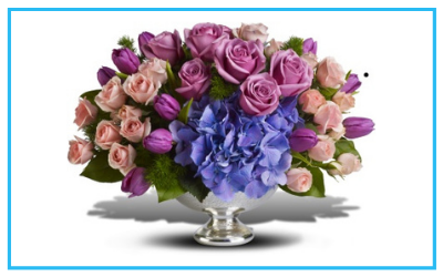 Bouquet of pink, purple, and blue flowers in a clear glass vase on a white background