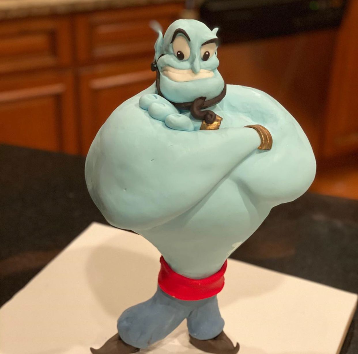 Blue cartoon genie figurine with arms crossed, sitting on a table indoors