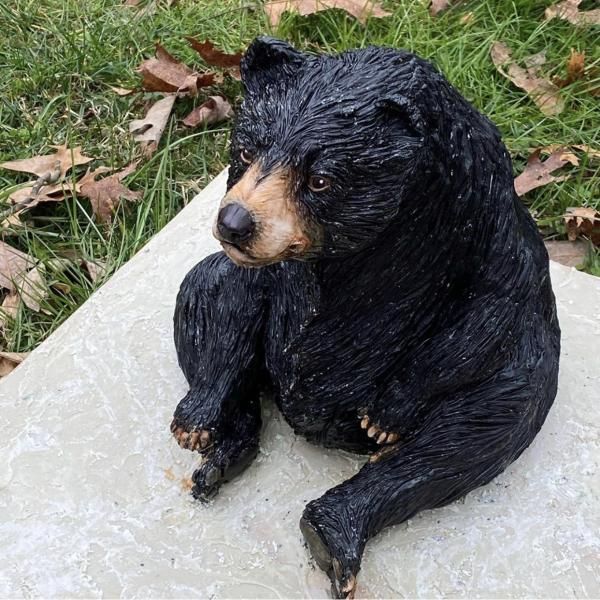 Small black dog figurine sitting on a stone slab in grass with autumn leaves nearby