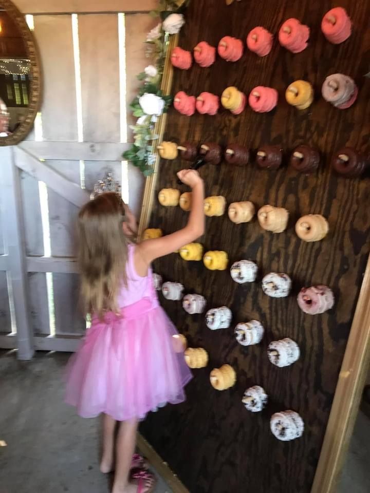 Girl in a pink dress reaching for donuts on a wooden wall display.