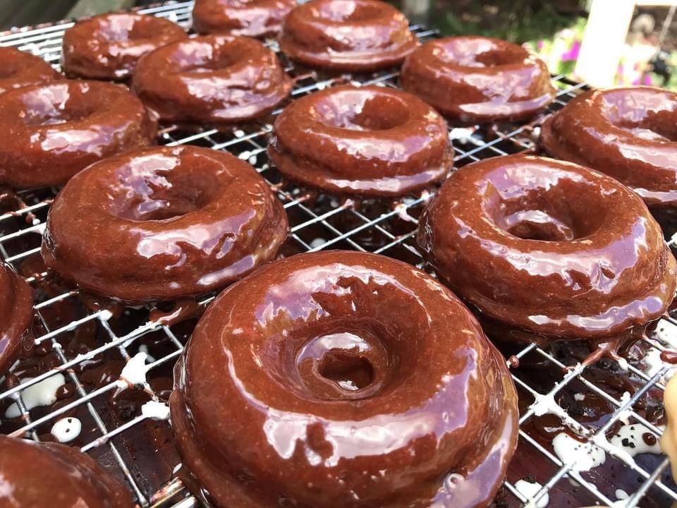 Glazed chocolate donuts cooling on a wire rack, with a glossy finish and one plain ring in front