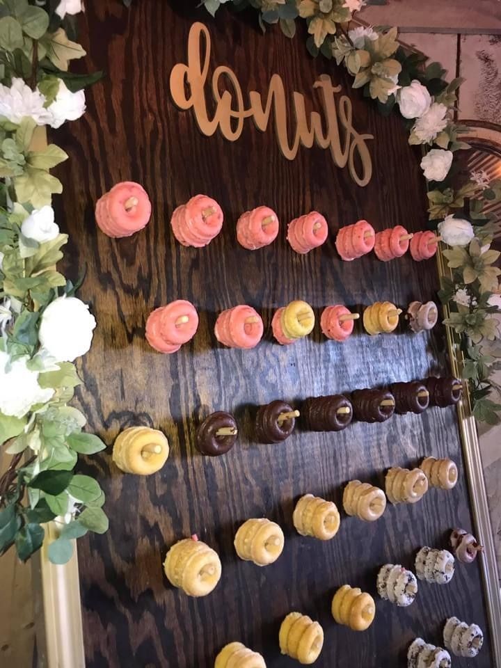 Floral dessert display with rows of colorful macarons under a wooden “donuts” sign
