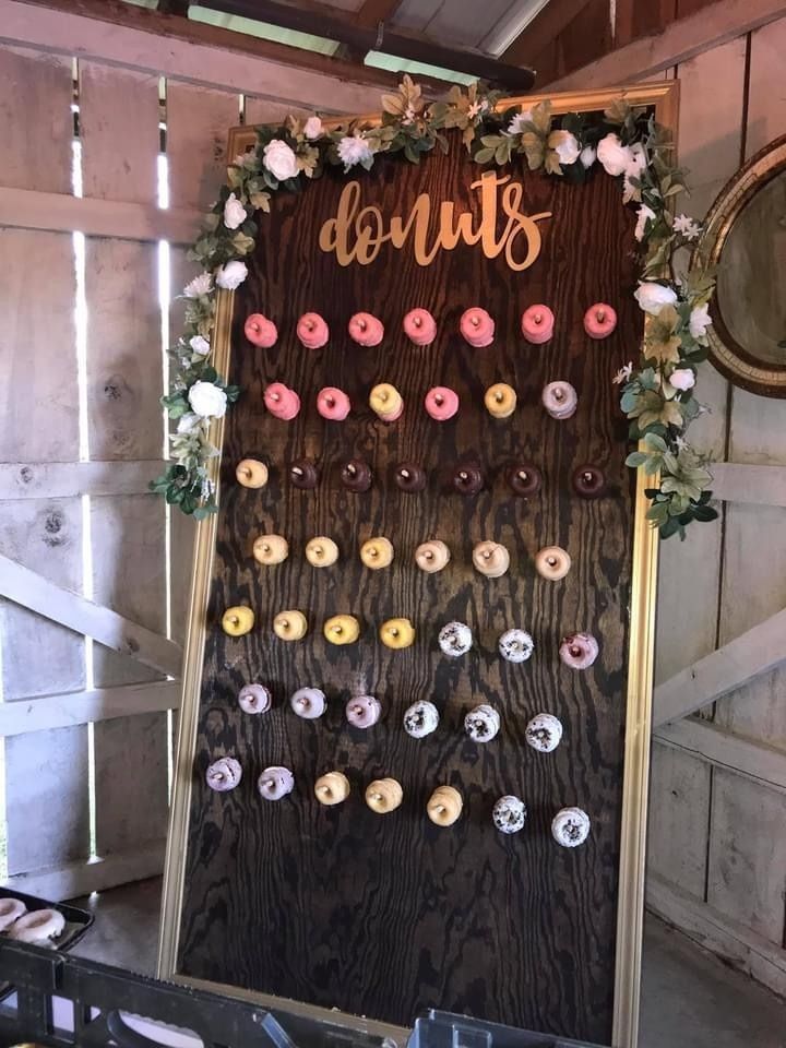 Donut display board with pink, white, and yellow donuts on a rustic wooden backdrop under floral decor