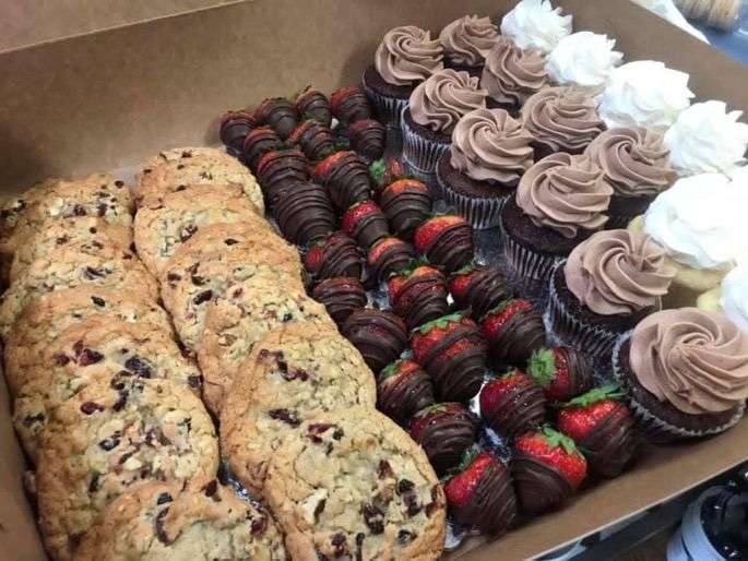 Assorted cookies, chocolate-dipped strawberries, and frosted cupcakes arranged in a pastry box